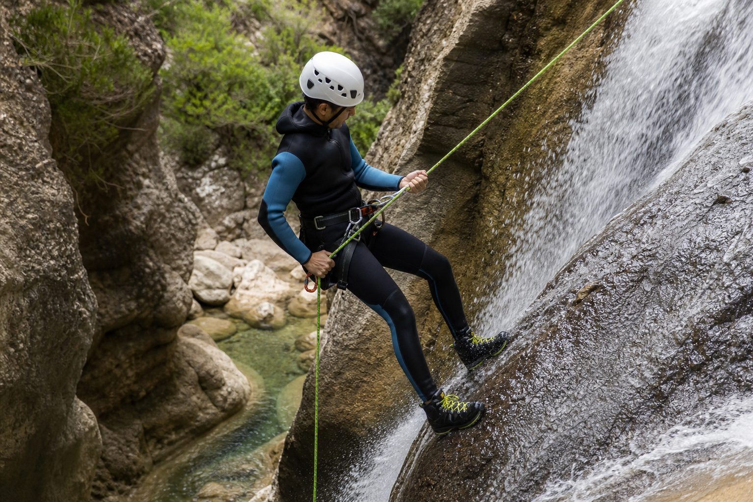 Deportista descendiendo en rápel junto a una cascada en un barranco de roca